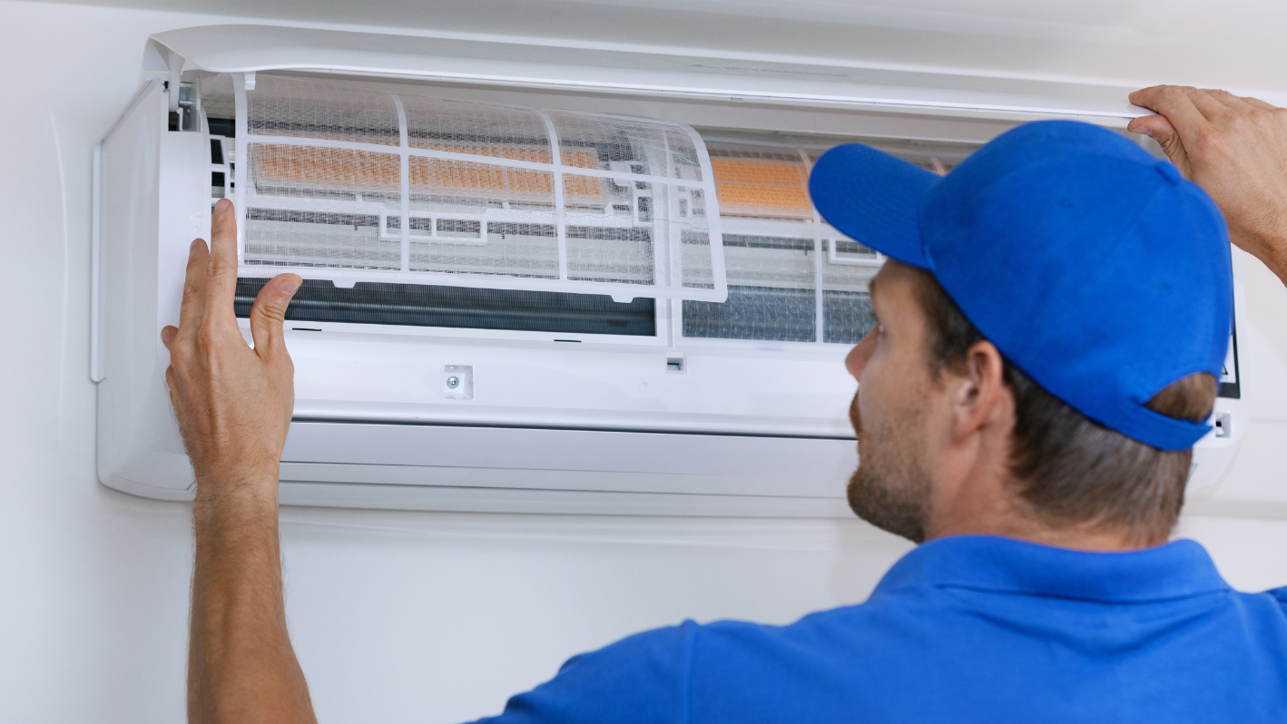 A man in a blue shirt and a blue cap working on an air conditioner